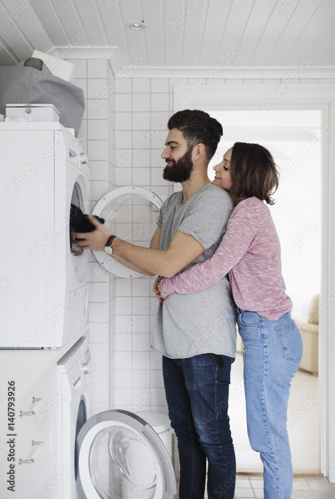 Woman embracing man while loading clothes in washing machine at home Woman embracing man while loading clothes in washing machine at home