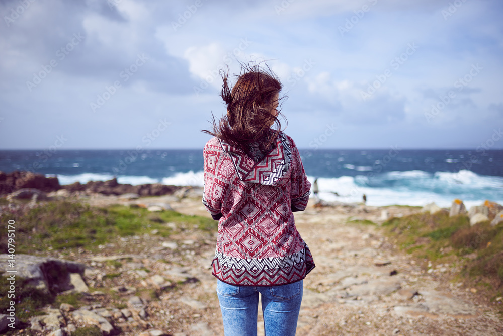 Mujer joven con un poncho contemplando el mar