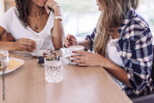 Two young and beautiful women meet at the bar for a cappuccino and to chat