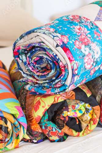 Three colored patchwork quilts twisted into close up. Colorful scrappy blankets folded as background. Handmade. DOF.