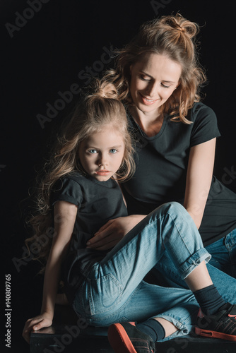 stylish smiling mother hugging daughter on black © LIGHTFIELD STUDIOS