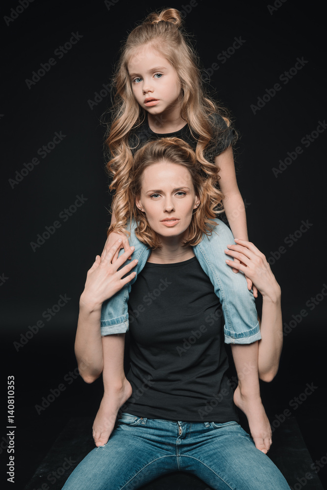 front view of daughter sitting on mother's shoulders on black front view of daughter sitting on mother's shoulders on black