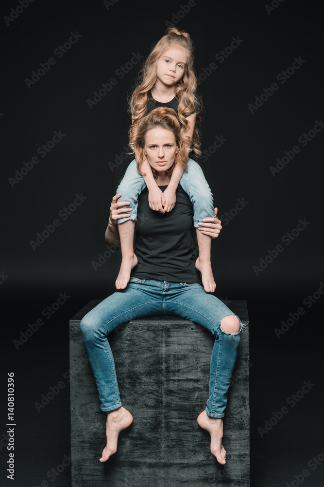 front view of daughter sitting on mother's shoulders on black front view of daughter sitting on mother's shoulders on black