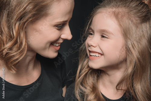 portrait of stylish daughter and mother smiling and looking at each other on black © LIGHTFIELD STUDIOS