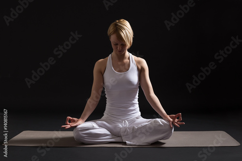 Woman exercising yoga indoor on black background,Lotus position/Padmasana