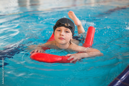 boy  swimming with a red foam noodle in a indoor pool
