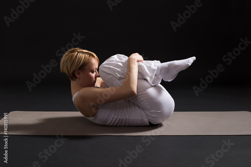 Woman exercising yoga indoor on black background,Wind Relieving pose/Pawanmuktasana photo