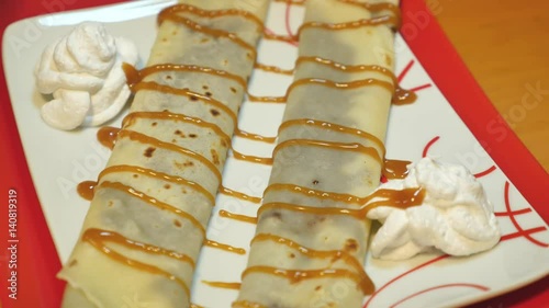 A person decorates two pancakes on a white plate with a caramel cream...
