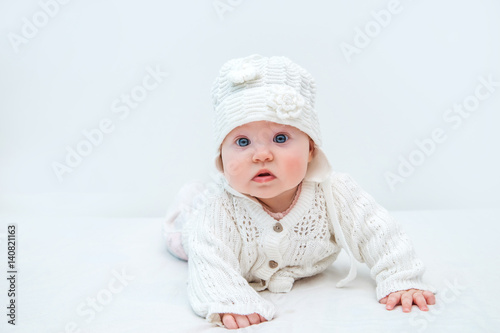 Cute baby in white knitted hat and sweater on a white background.