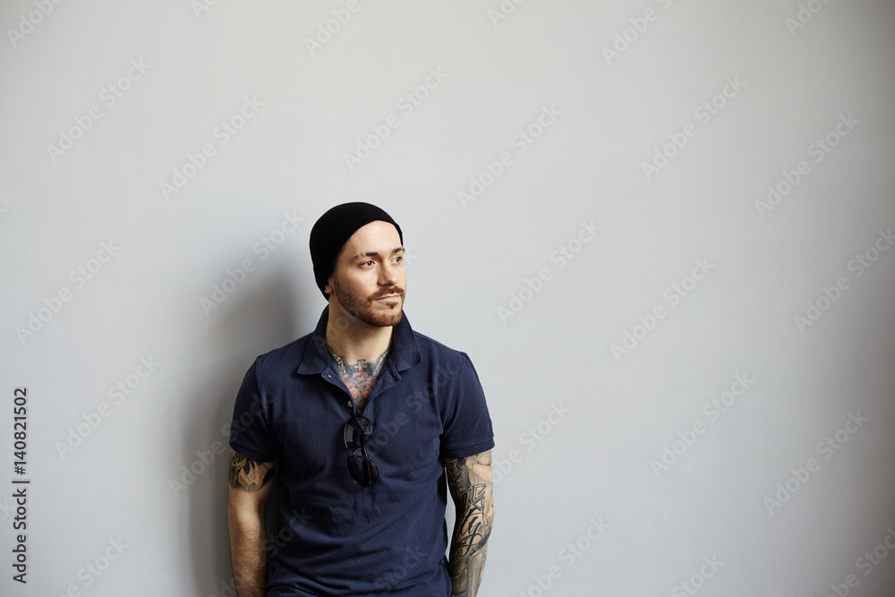 handsome latin man with tattooed body in dark blue polo and black hat. Glad person. Guy look away to the right side. Confident designer thinking new idea for loft interior. handsome latin man with tattooed body in dark blue polo and black hat. Glad person. Guy look away to the right side. Confident designer thinking new idea for loft interior.