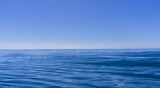 Abstract background deep blue oily looking surface of ocean in motion defocused with hazy sea shimmer and sky on horizon