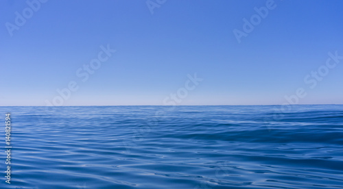 Abstract background deep blue oily looking surface of ocean in motion defocused with hazy sea shimmer and sky on horizon