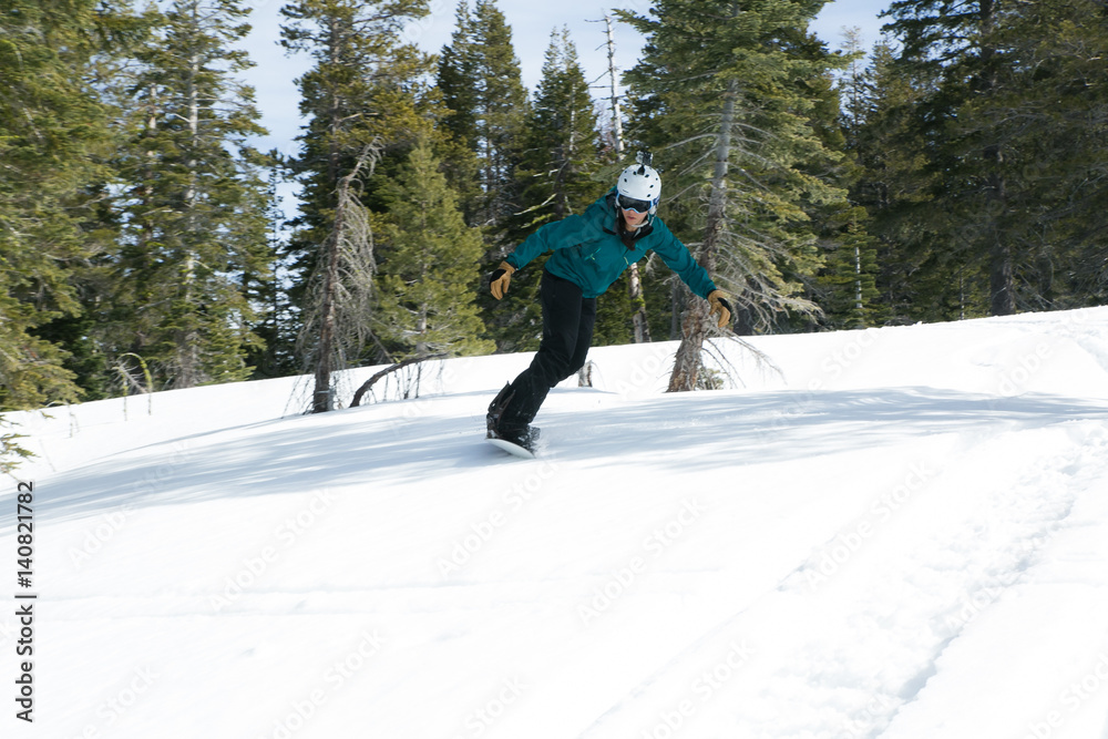 Young woman snowboards in a forested backcountry in Lake Tahoe, California