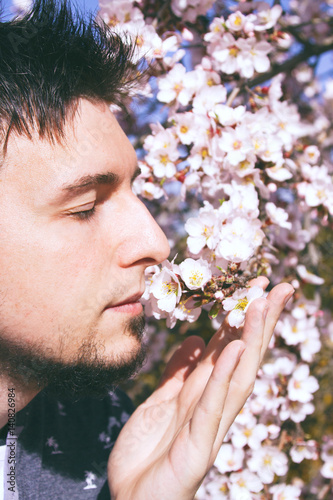 Hombre joven disfrutando del aroma de las flores de almendro en primavera photo
