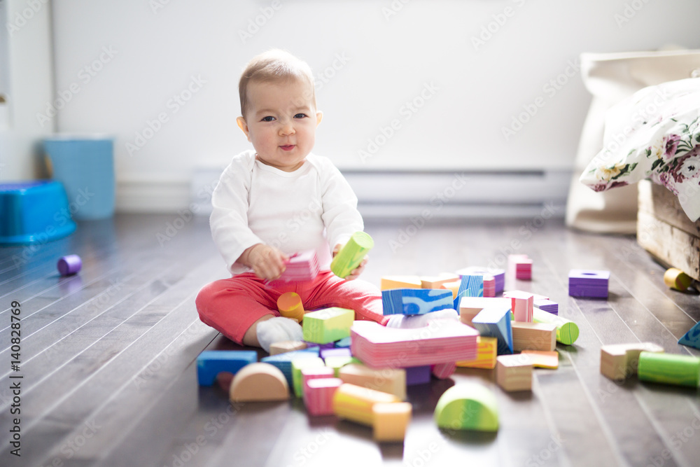 Cute little baby girl play with plastic bricks sitting indoors on a tiles floor Cute little baby girl play with plastic bricks sitting indoors on a tiles floor