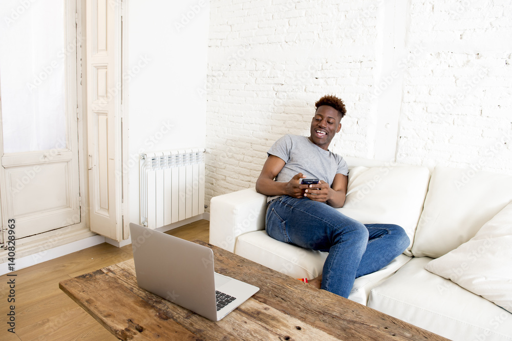 black man sitting at home sofa couch working with laptop computer and mobile phone