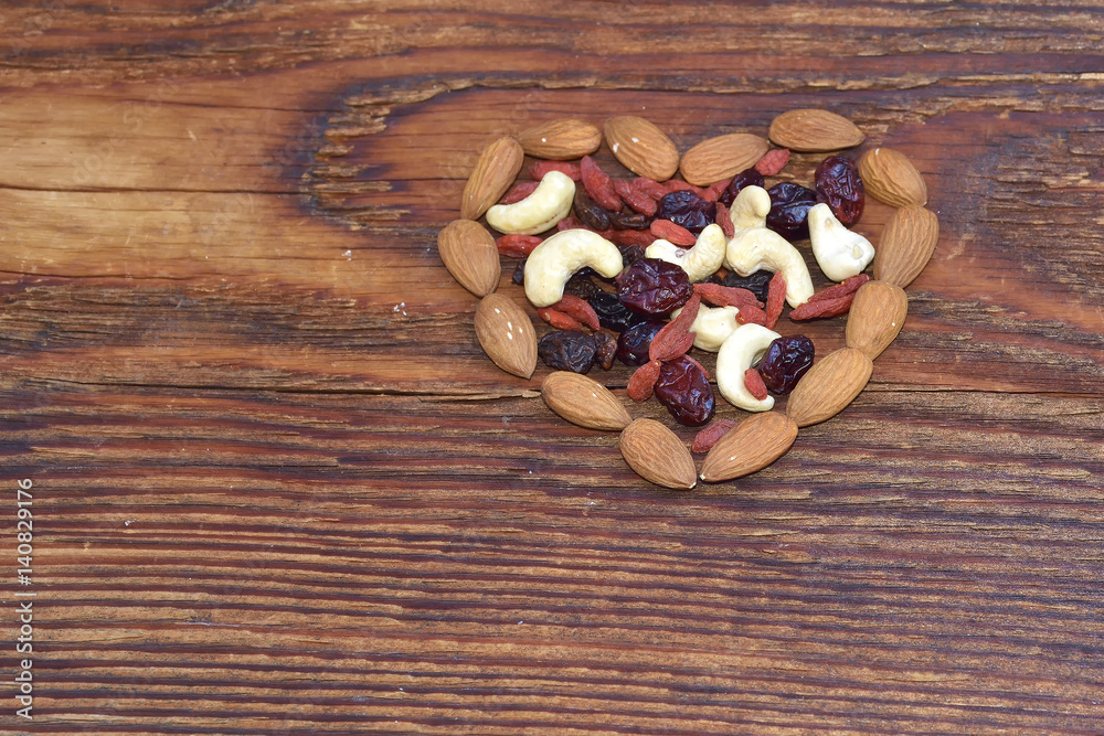 Mixed nuts and dried fruits forming a heart-shape on wood background Mixed nuts and dried fruits forming a heart-shape on wood background