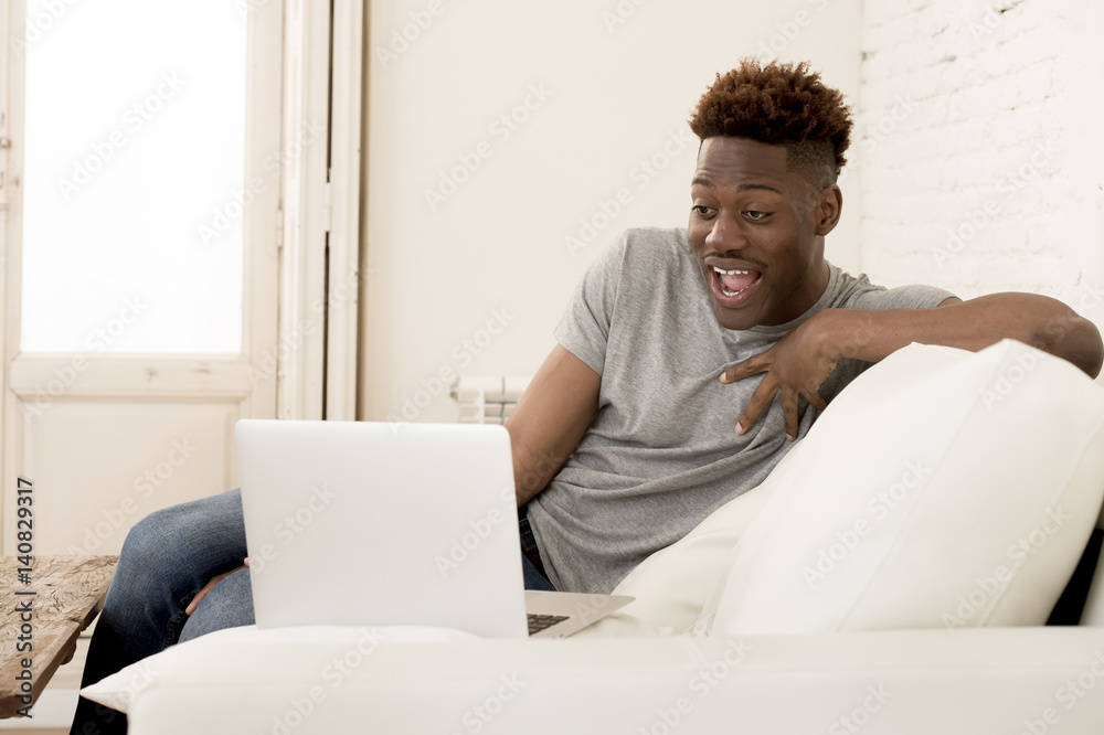 happy black man sitting at home sofa couch working or enjoying internet movie in laptop happy black man sitting at home sofa couch working or enjoying internet movie in laptop