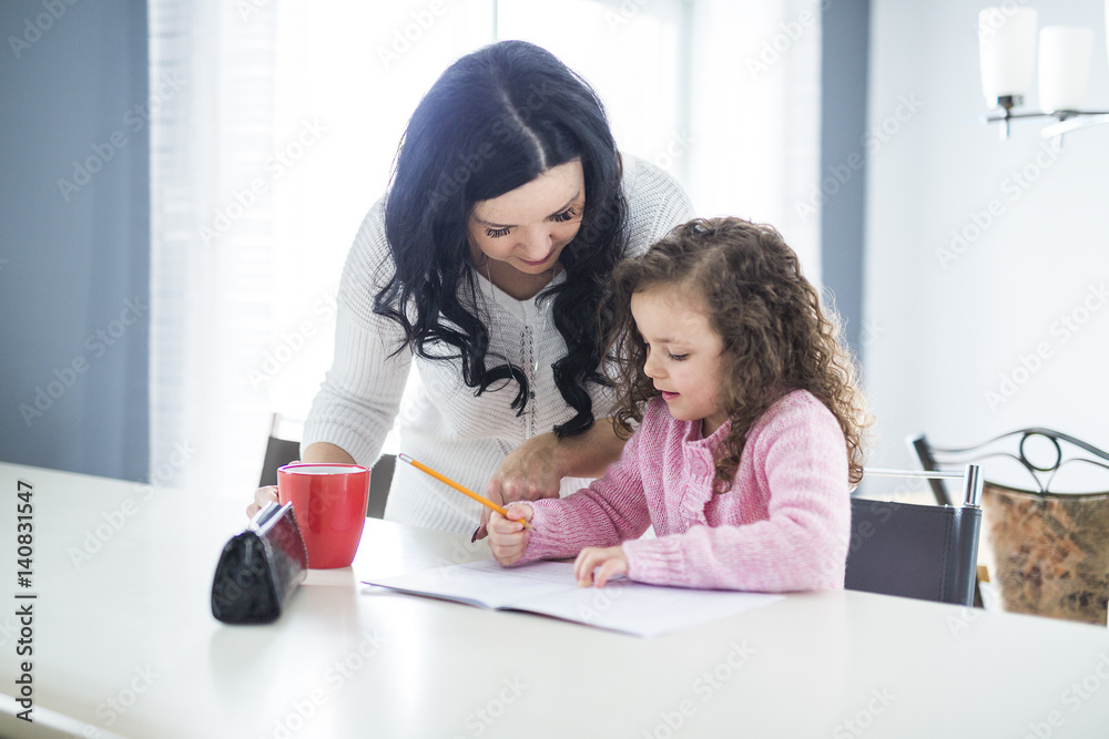 Beautiful school girl doing homework with mother at home Beautiful school girl doing homework with mother at home