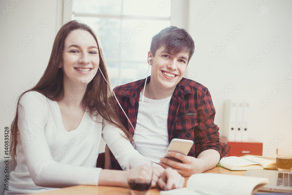 Young Adults, studying and having Fun at home, Listening to music on the Smartphone together Young Adults, studying and having Fun at home, Listening to music on the Smartphone together