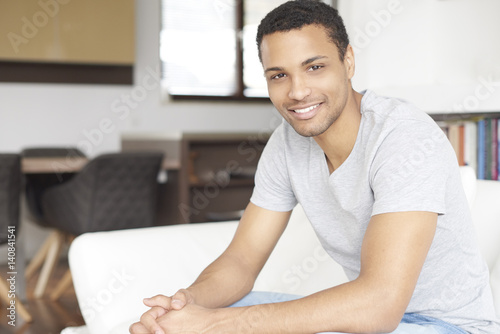 Free Download Enjoy my life. Shot of an African American young man relaxing at home on the sofa while looking at camera and smiling. - GFXLoad