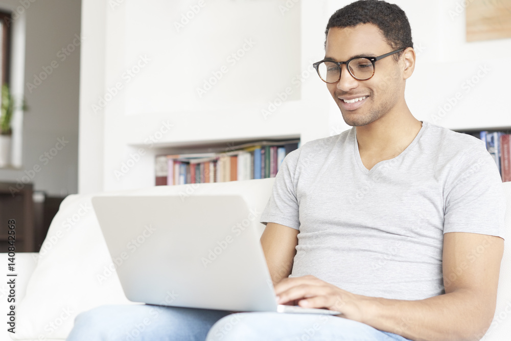 Browsing on the internet. full length shot of a smiling young afro American man using a laptop while relaxing in his living room at home. Browsing on the internet. full length shot of a smiling young afro American man using a laptop while relaxing in his living room at home.