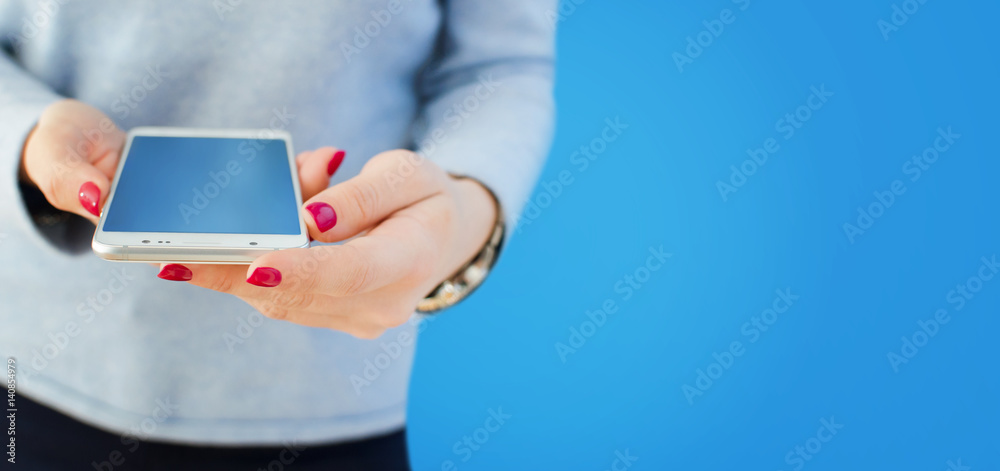 Angled view of modern phone in female hands with empty light blue screen, on light blue background Angled view of modern phone in female hands with empty light blue screen, on light blue background