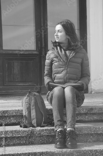 A beautiful young woman sitting on stairs with book outside