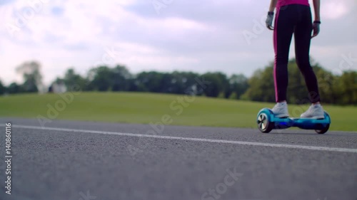 Woman rides gyroscooter on park road. Girl using self balancing gyro scooter. Back view of woman on electric hover board. Woman drive dual wheel personal electric scooter. Future transport photo