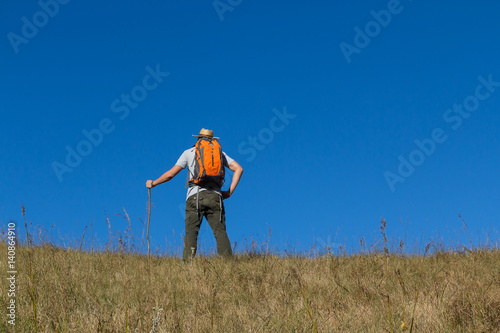 Man with backpacks trekking to the hill with blue sky background.