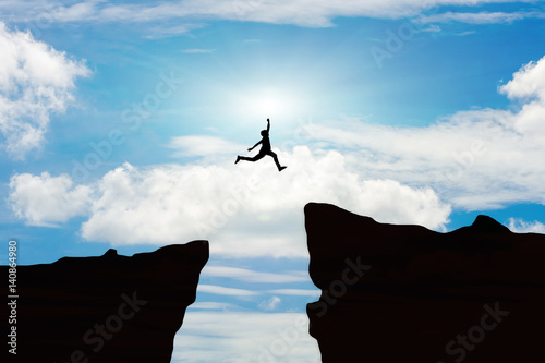Man jump through the gap between hill.man jumping over cliff on sunset background,Business concept idea