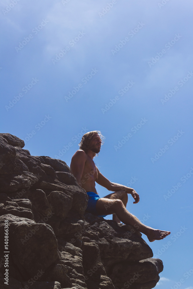The person sitting at the rock. Side view of a climber sitting at the rock and looking away. Vertical outdoors shot. The person sitting at the rock. Side view of a climber sitting at the rock and looking away. Vertical outdoors shot.