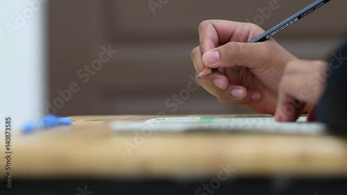 Student holding pencil for exam and filling answer on papersheet in test classroom at highschool  photo