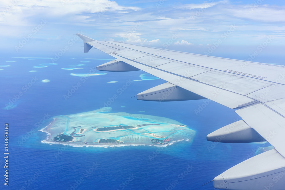 Scenery from airplane 's window seeing wing of airplane , white clouds , blue sky and Maldives islands