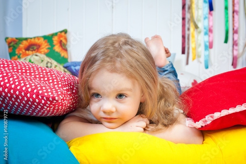Sweet smiling girl 3-4 years sitting on the floor among the colored pillows