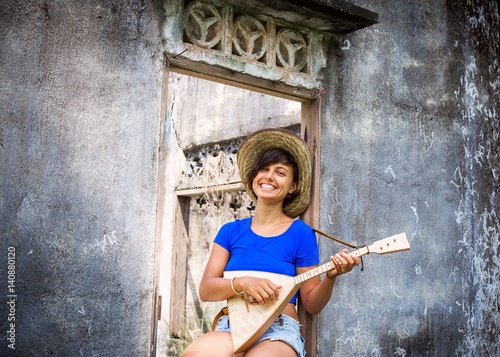 Woman playing music with balalaika at grey wall background.