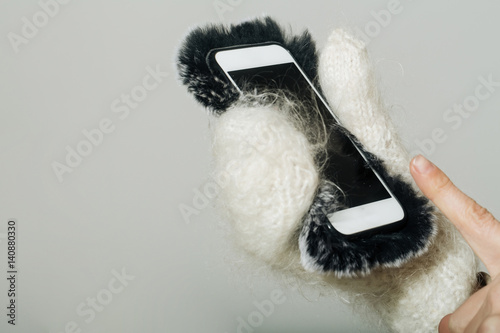 Female hand in white mittens holding smartphone in fur cover