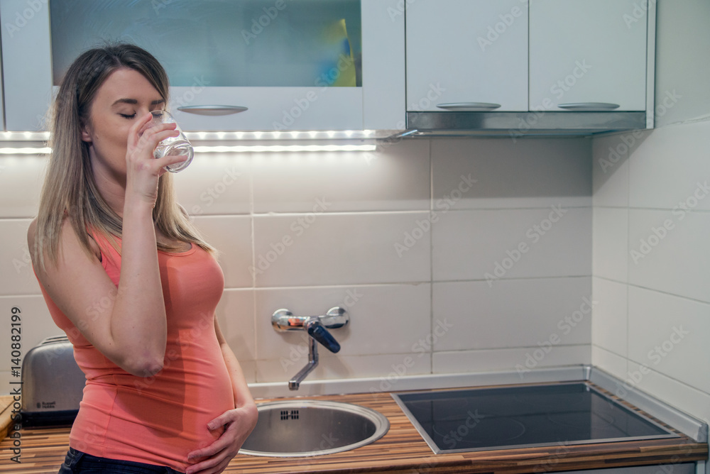 Pregnant woman with glass of water in hand, concept of healthy lifestyle, nutrition and hydration in pregnancy. Happy pregnant woman holding a glass of water while standing in the kitchen Pregnant woman with glass of water in hand, concept of healthy lifestyle, nutrition and hydration in pregnancy. Happy pregnant woman holding a glass of water while standing in the kitchen