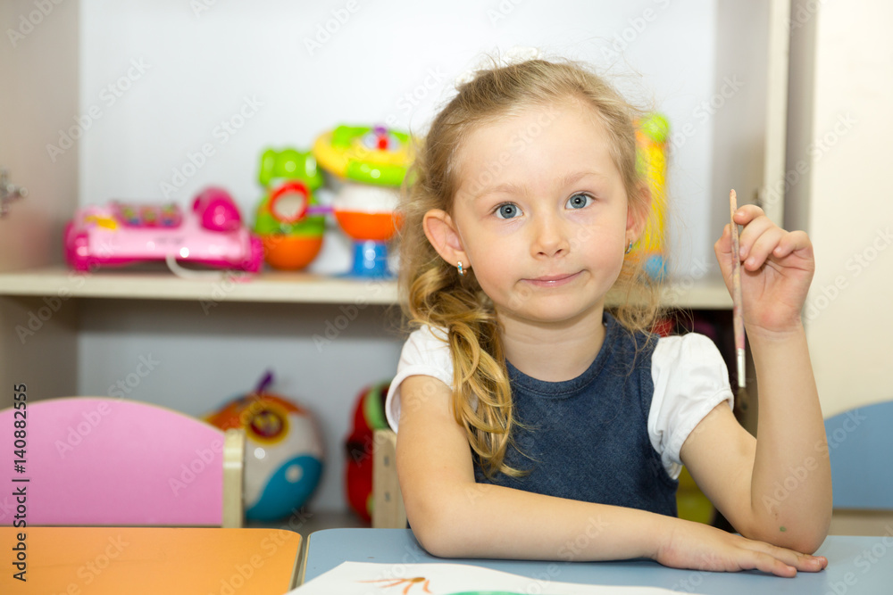 Adorable child girl draws a brush and paints in nursery room. Kid in kindergarten in Montessori preschool class. Adorable child girl draws a brush and paints in nursery room. Kid in kindergarten in Montessori preschool class.