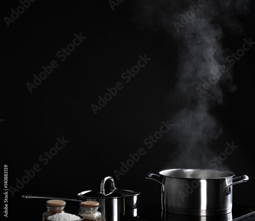 Saucepan with steam on black background