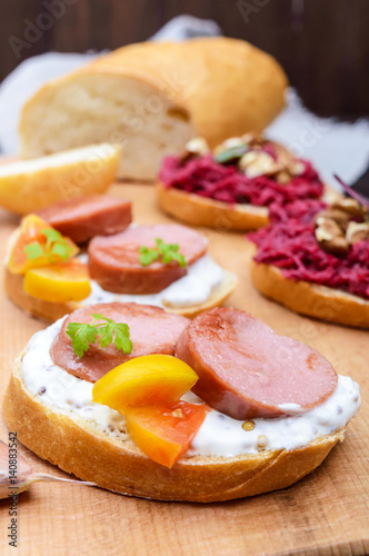 Sandwiches for breakfast with fried sausages, yellow tomatoes, creamy mustard sauce on a cutting board. Vertical view