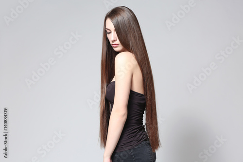 Beautiful young woman with long straight hair on light background