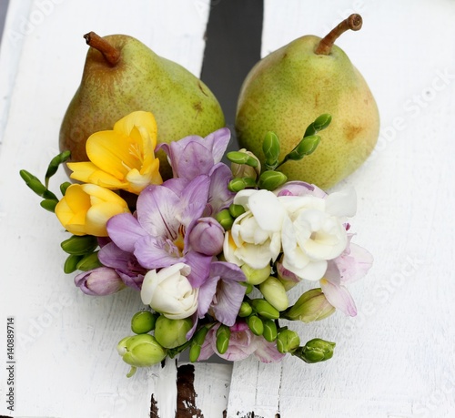 Two ripe pears and a posy of scented spring freesia on a white wooden vintage crate 