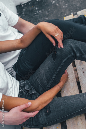 Young happy couple sitting outside a cafe on the street on the floor. Close-up of jeans on legs model.