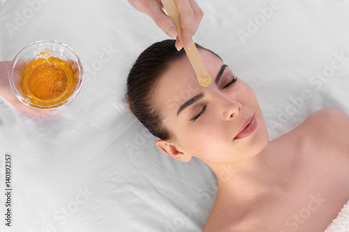 Beautician depilating young woman's face with wax in spa center