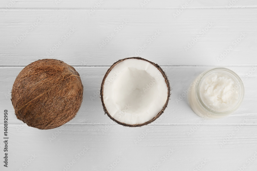 Fresh coconut and glass jar with oil on white wooden background
