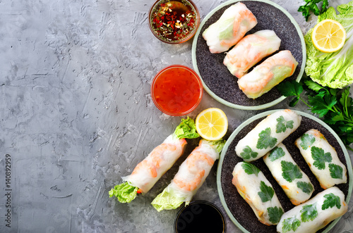 Fresh Vietnamese, Asian, Chinese food frame on grey concrete background. Spring rolls rice paper, lettuce, salad, vermicelli, noodles, shrimps, fish sauce, sweet chili, soy, lemon. Top view.