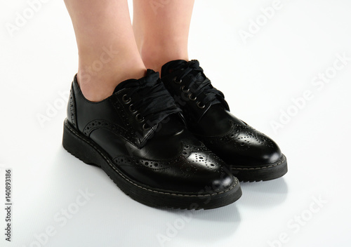 Legs in stylish black brogue shoes on light background