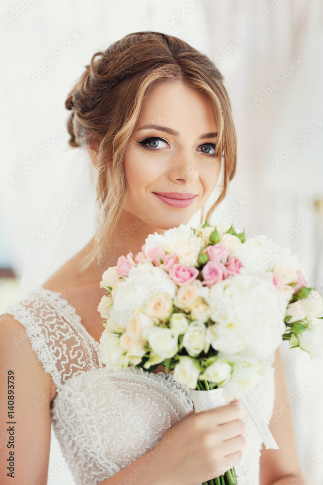 Gorgeous bride with broad smile holds wedding bouquet before her face