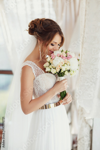 Bride in dress with laces smells her bouquet standing in the room
